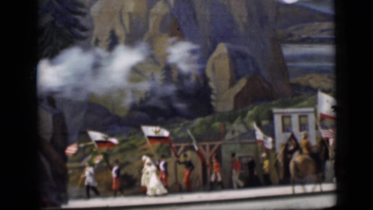 Miniature train and costumed parade figures pass a painted Western backdrop with smoke.