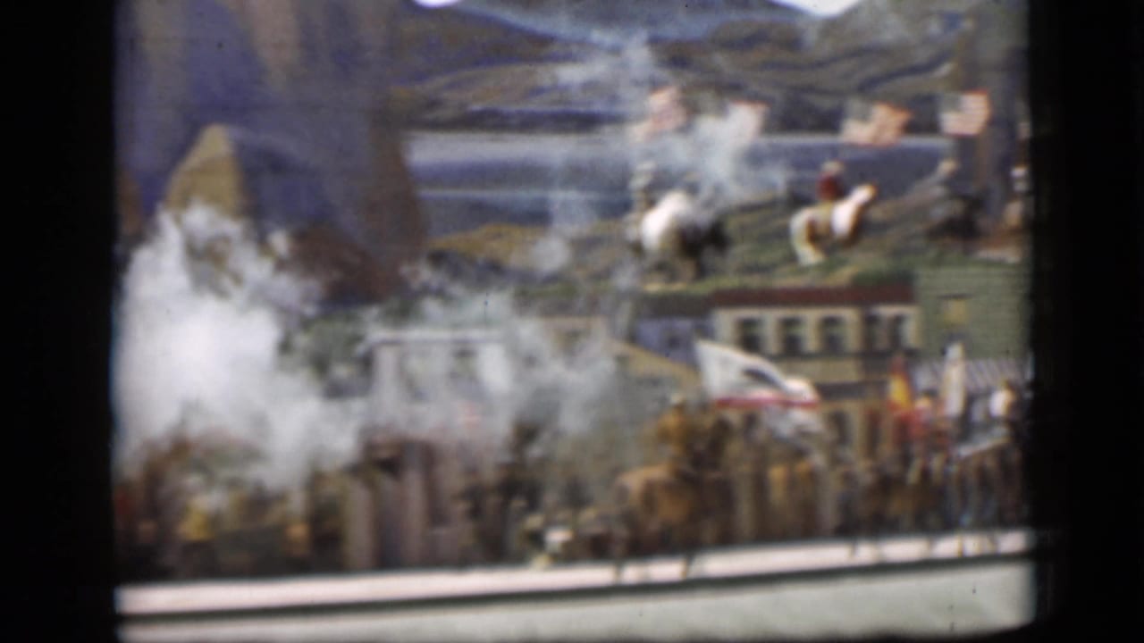 Smoke rises in front of horseback riders, flags, and a Western town backdrop.