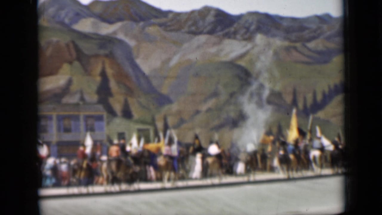 A line of riders, flags, and costumed parade participants fills the frame before a painted mountain backdrop in San Francisco.