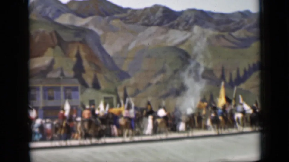 A line of riders, flags, and costumed parade participants fills the frame before a painted mountain backdrop in San Francisco.