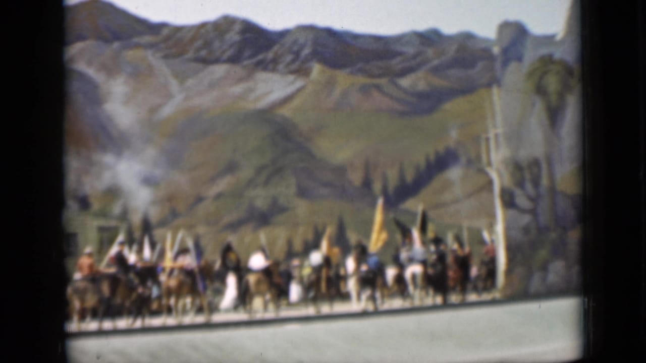 Horseback riders and marchers pass before a painted mountain backdrop with flags visible.
