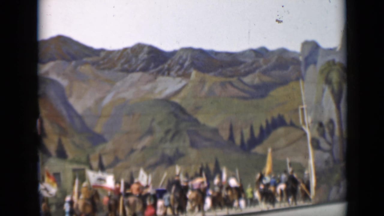 1937 San Francisco home-movie frame of horseback participants and flag bearers passing a painted mountain and valley backdrop.