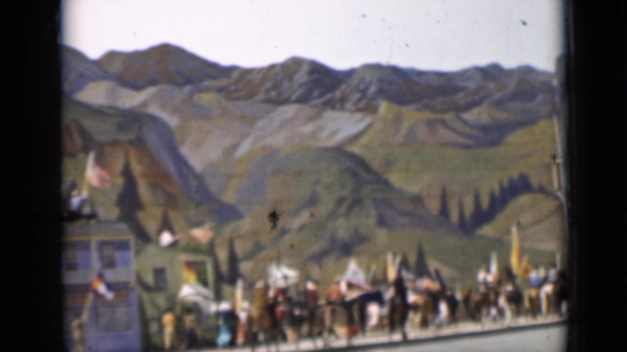 1937 San Francisco frame showing riders, pedestrians, and flags in a parade scene with painted mountains behind them.
