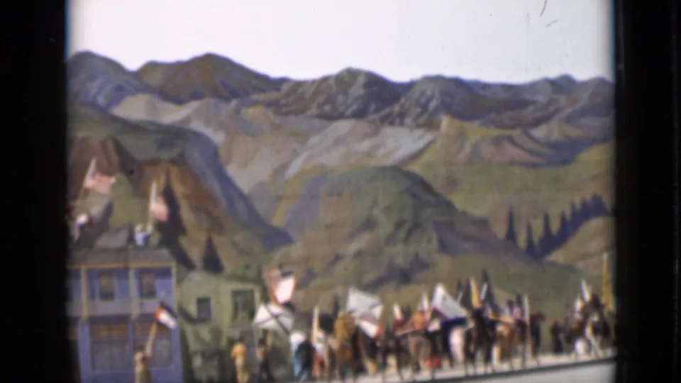 1937 San Francisco 8mm frame showing a staged horseback procession with flags before false-front buildings and painted mountains.
