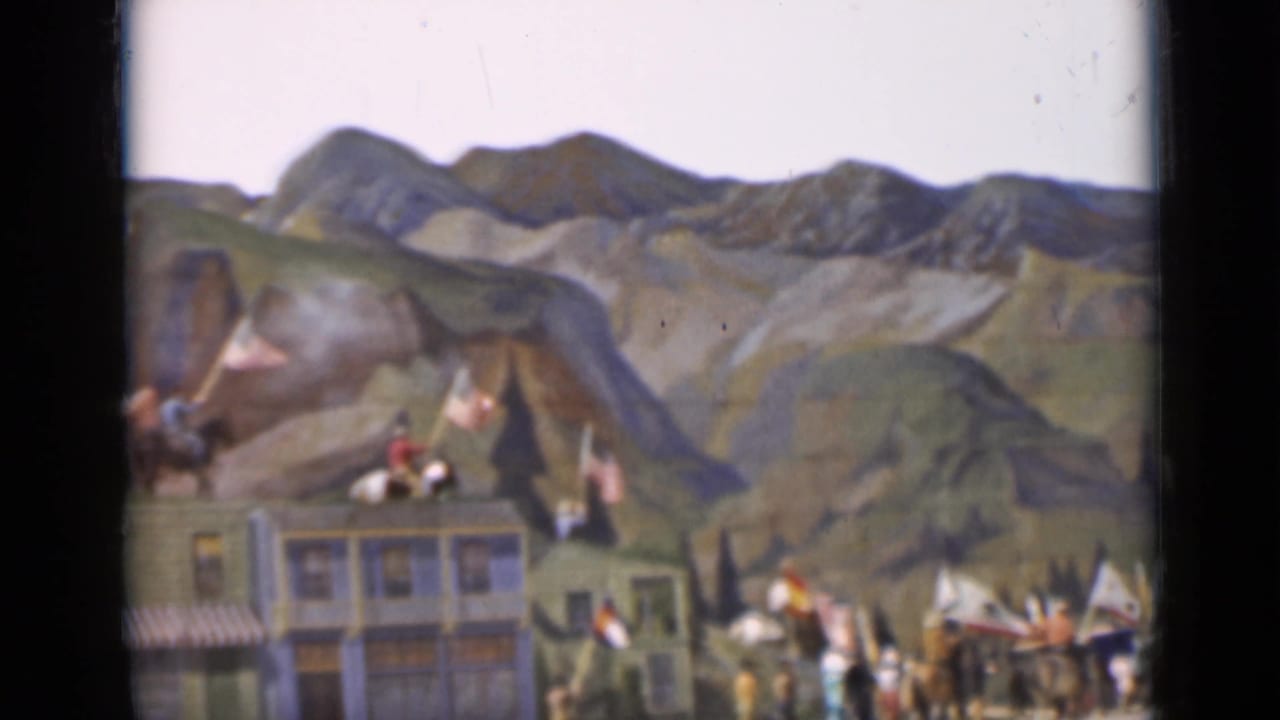 1937 San Francisco 8mm frame with mounted figures, flags, and costumed performers against a painted Western mountain setting.