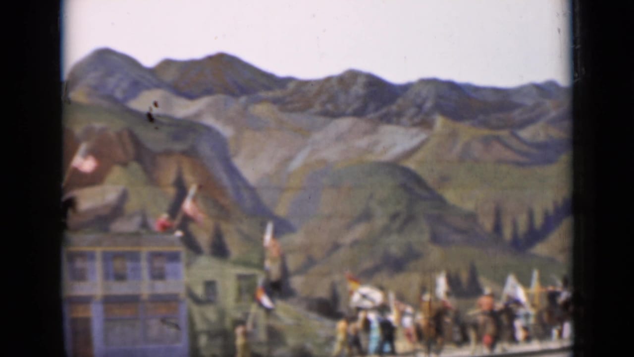 1937 San Francisco 8mm frame showing a soft, distant view of a staged march below a painted mountain backdrop.