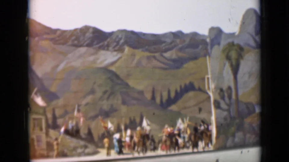 1937 San Francisco 8mm frame showing the procession near a road, with riders, flags, buildings, and painted scenery visible.
