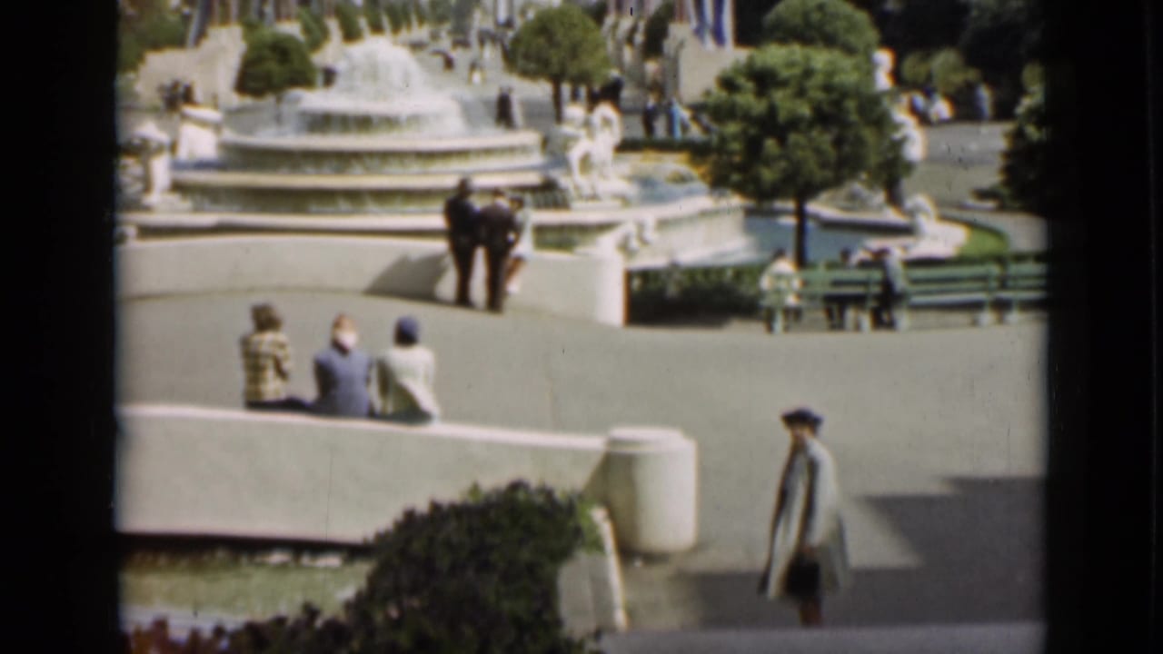 1937 San Francisco park scene with visitors seated and strolling near a tiered fountain, benches, clipped trees, and paved walkways.