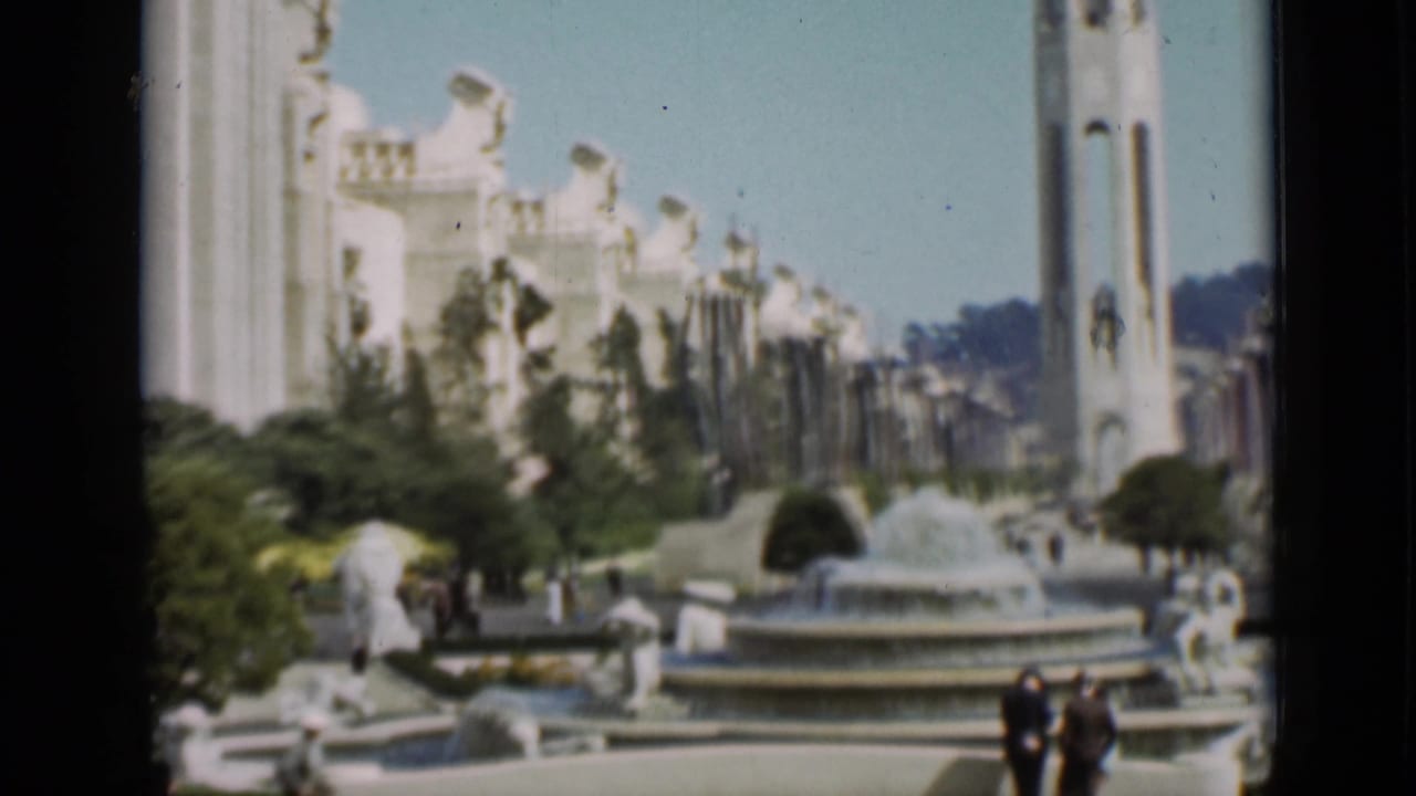 San Francisco exposition plaza showing a circular fountain, sculptural figures, the Tower of the Sun, white buildings, and visitors walking nearby.