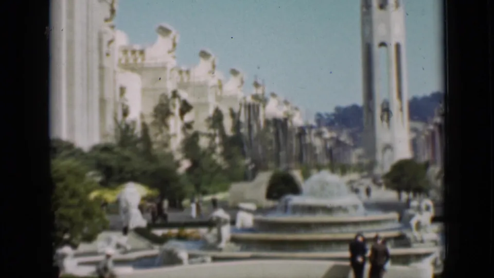 San Francisco exposition plaza showing a circular fountain, sculptural figures, the Tower of the Sun, white buildings, and visitors walking nearby.