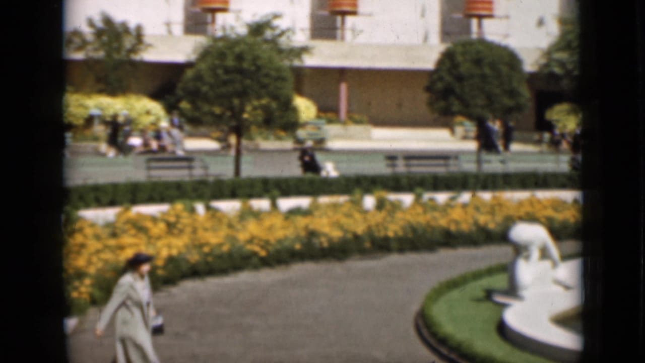 A curving plaza path passes yellow flower beds and white fountain sculpture as visitors walk through the 1937 San Francisco scene.