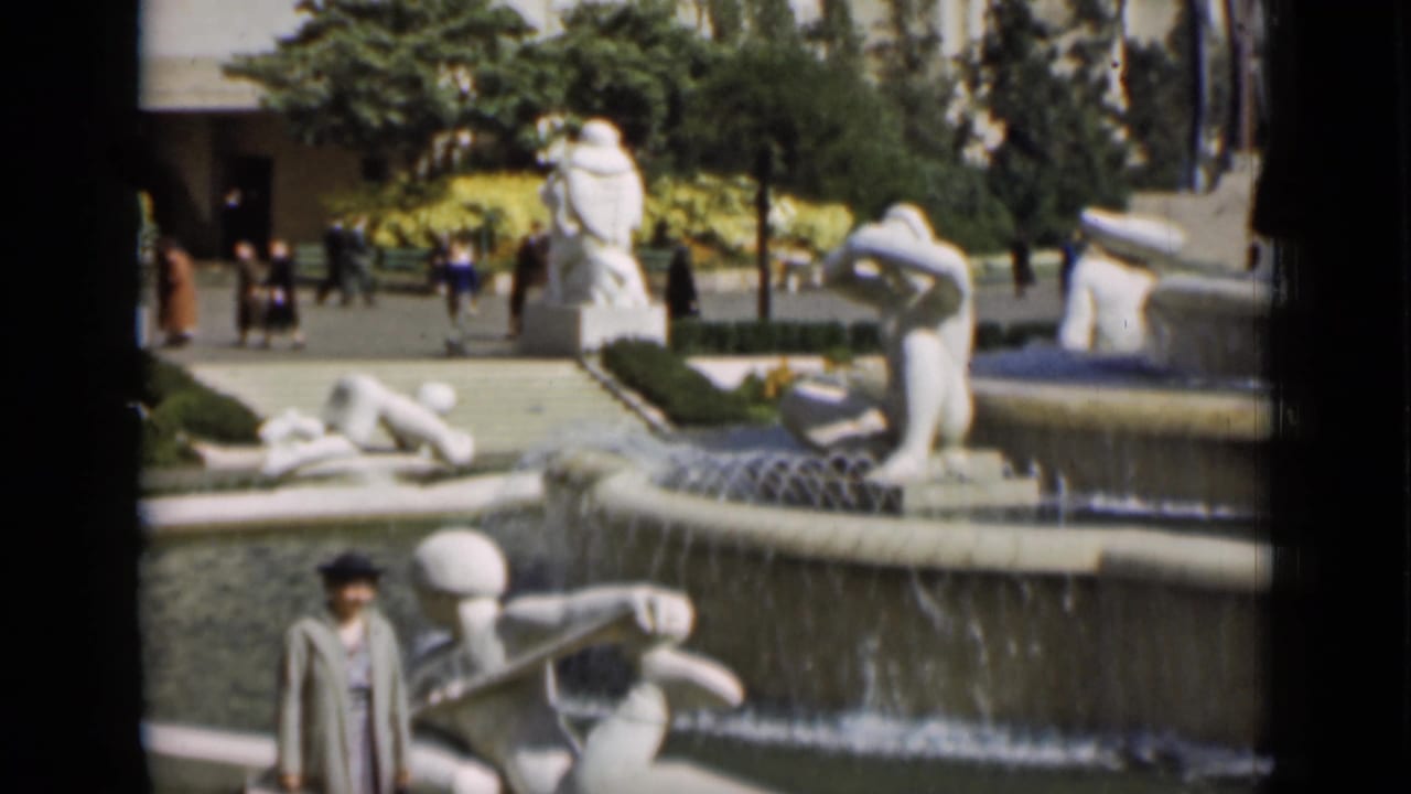 Stone fountain with white sculptural figures and a visitor walking in the foreground.