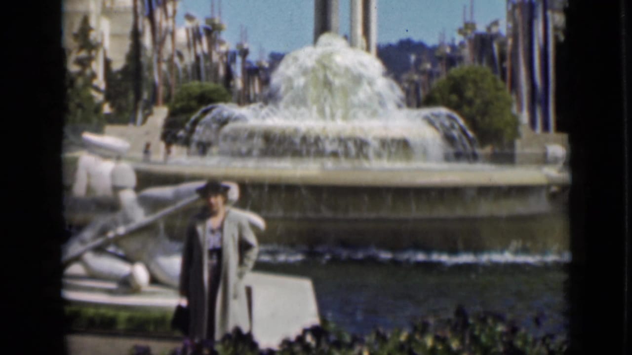 1937 San Francisco frame with a man in a long coat near the sculptural fountain, with a broad spray of water behind him.