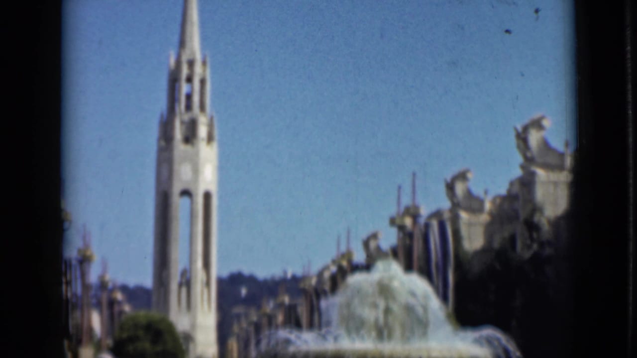1930s San Francisco footage frames a tall white spire near a fountain, with ornamental structures and hills in the distance.