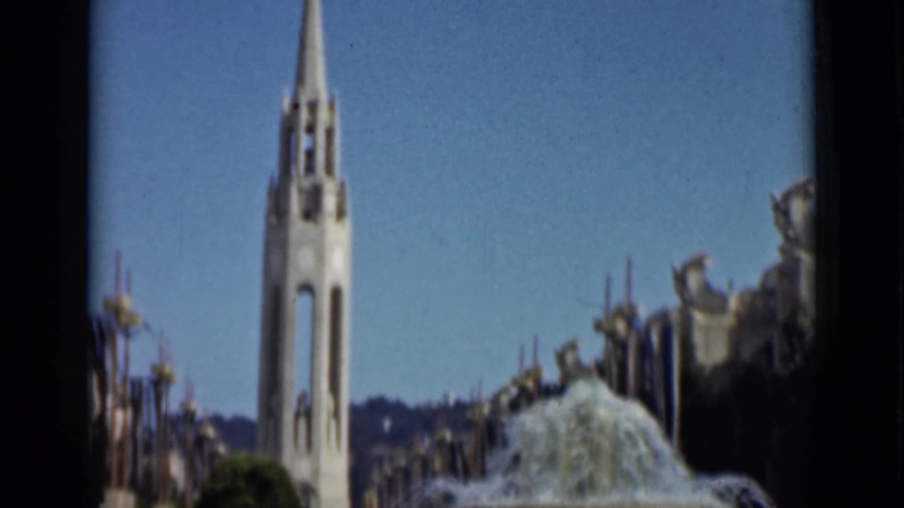 The home-movie view tilts toward the white spire, with fountain water and decorative civic architecture below.