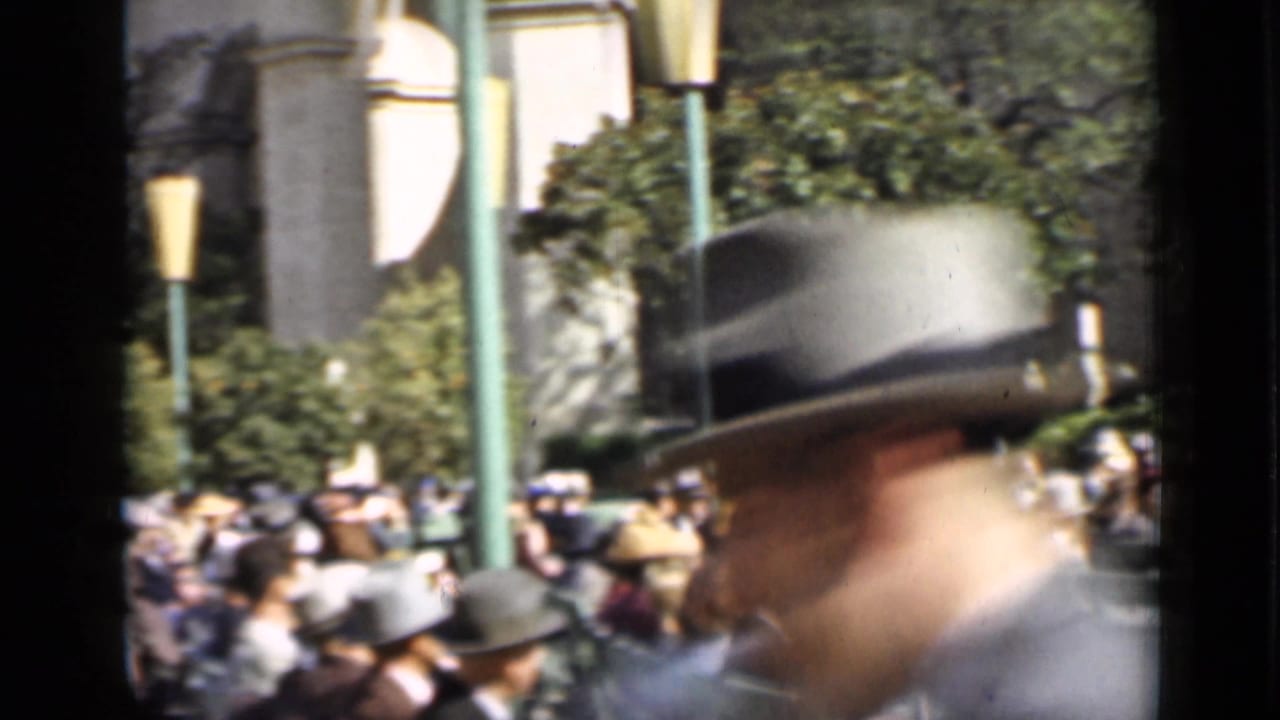 Crowd seated in green bleachers with a blurred man in a hat crossing the foreground.