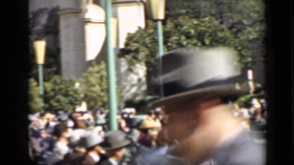 1937 San Francisco home-movie frame showing seated spectators in green bleachers as a man in a fedora passes close to the lens.