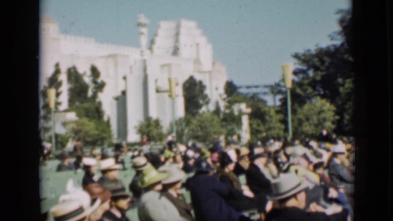 1937 San Francisco frame of spectators in green bleachers facing toward an event area near a pale Art Deco-style building and trees.