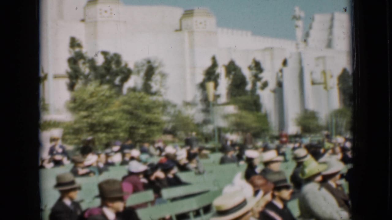 1937 San Francisco home-movie view of adults in period hats seated on green benches before trees and a bright white Art Deco-style structure.