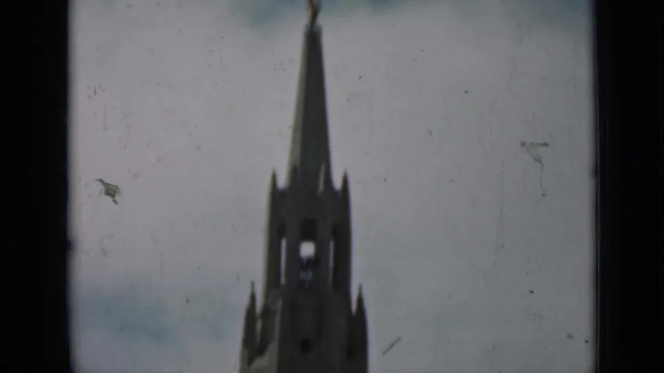 A soft-focus 8mm view shows a tall Gothic-style church or cathedral spire against a pale cloudy sky.