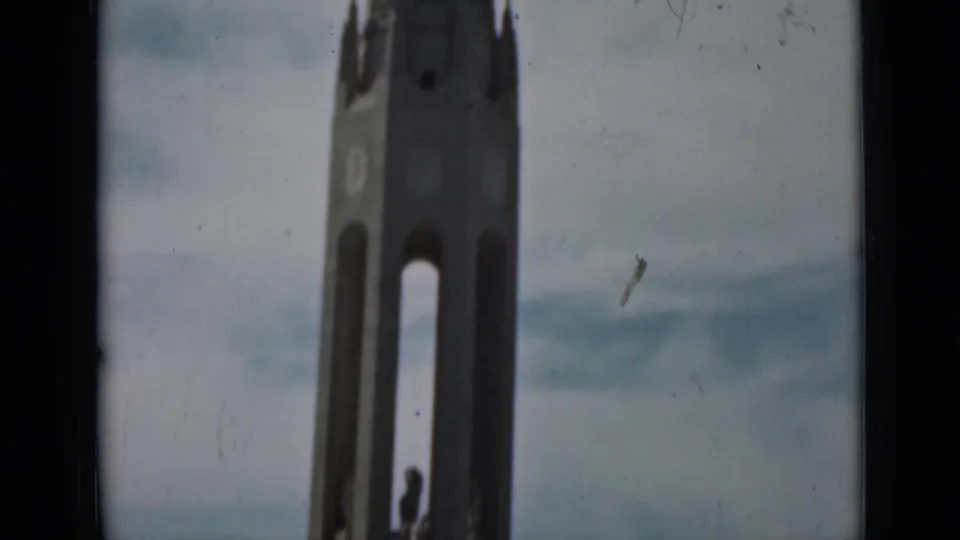 1937 San Francisco home-movie frame showing a tall monument tower, cloudy sky, and dark foreground edges.