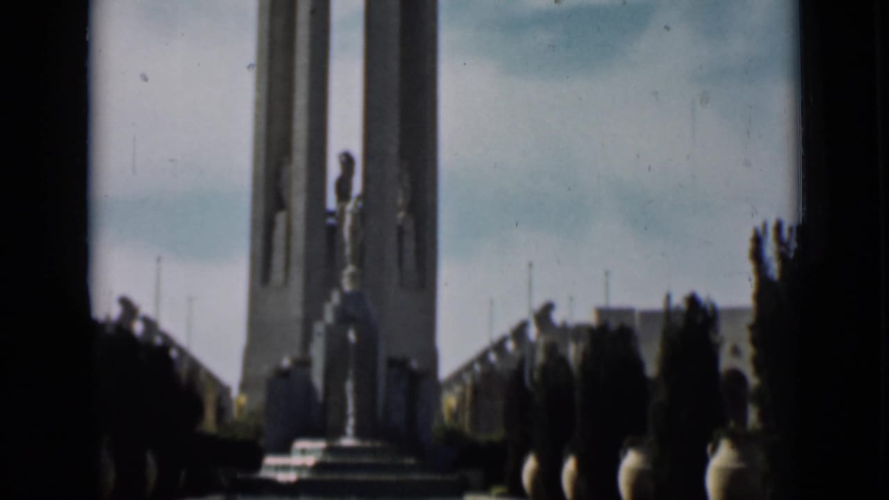 1937 San Francisco home-movie view of the tower monument with statue, steps, and silhouetted visitors at the edge.