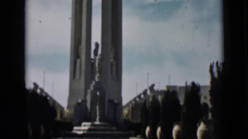 1937 San Francisco home-movie view of the tower monument with statue, steps, and silhouetted visitors at the edge.
