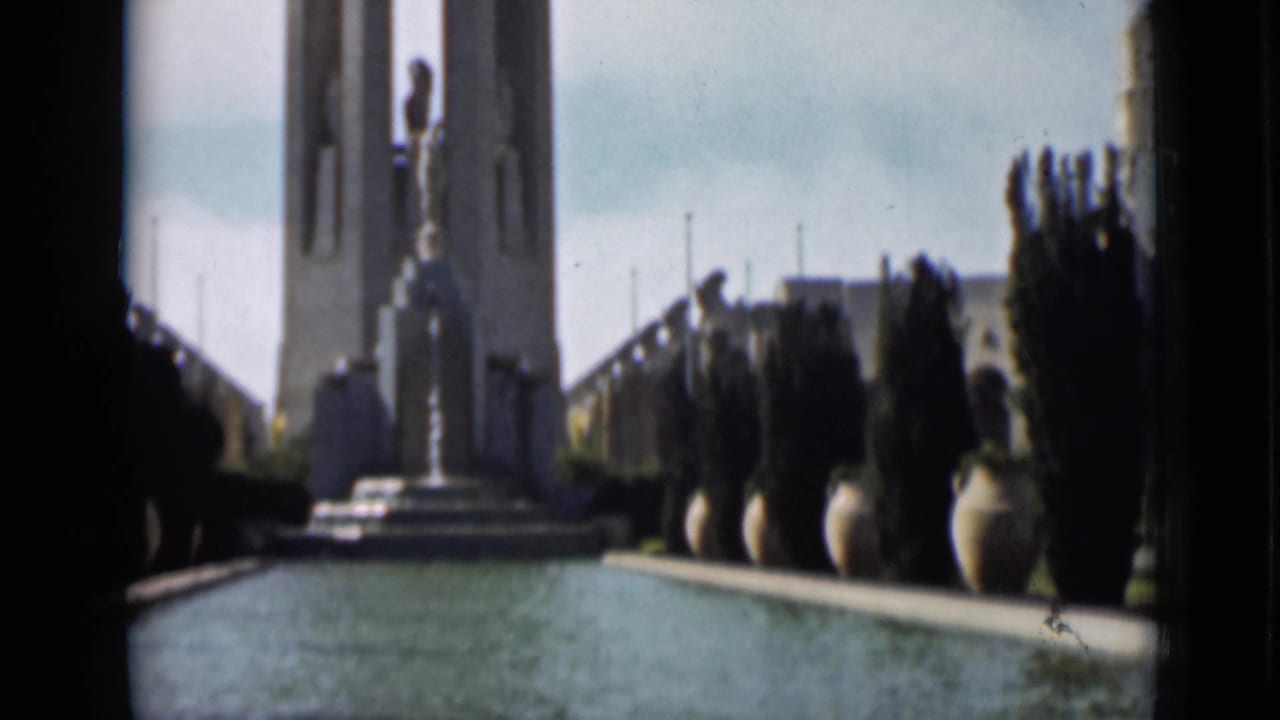 Wider 1937 San Francisco frame with reflecting pool, statue, tower, planters, and distant silhouetted visitors.
