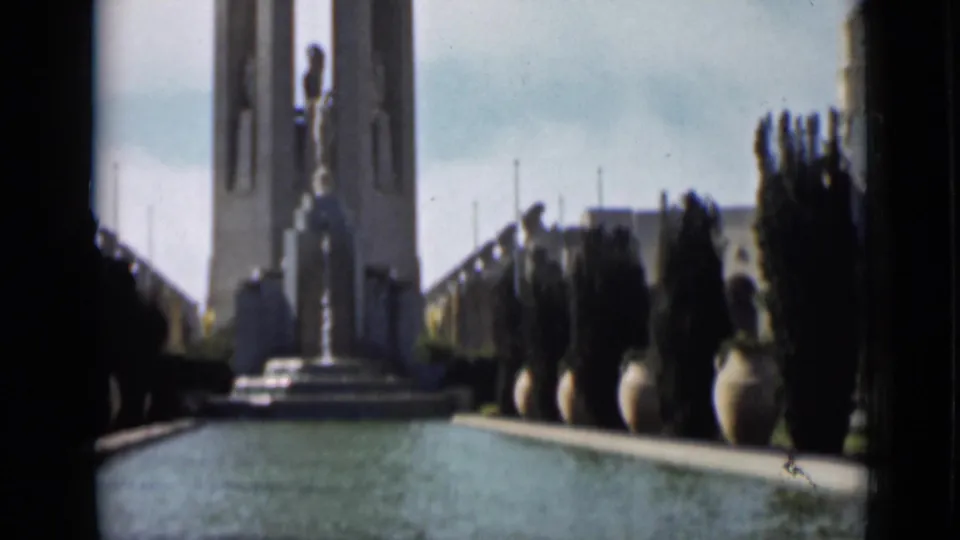 Wider 1937 San Francisco frame with reflecting pool, statue, tower, planters, and distant silhouetted visitors.