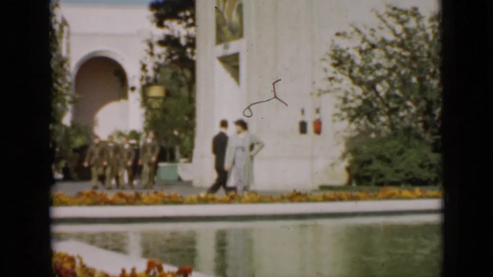 Uniformed men gather near a white arched building while two pedestrians pass beside the reflecting pool in this 1937 San Francisco garden scene.