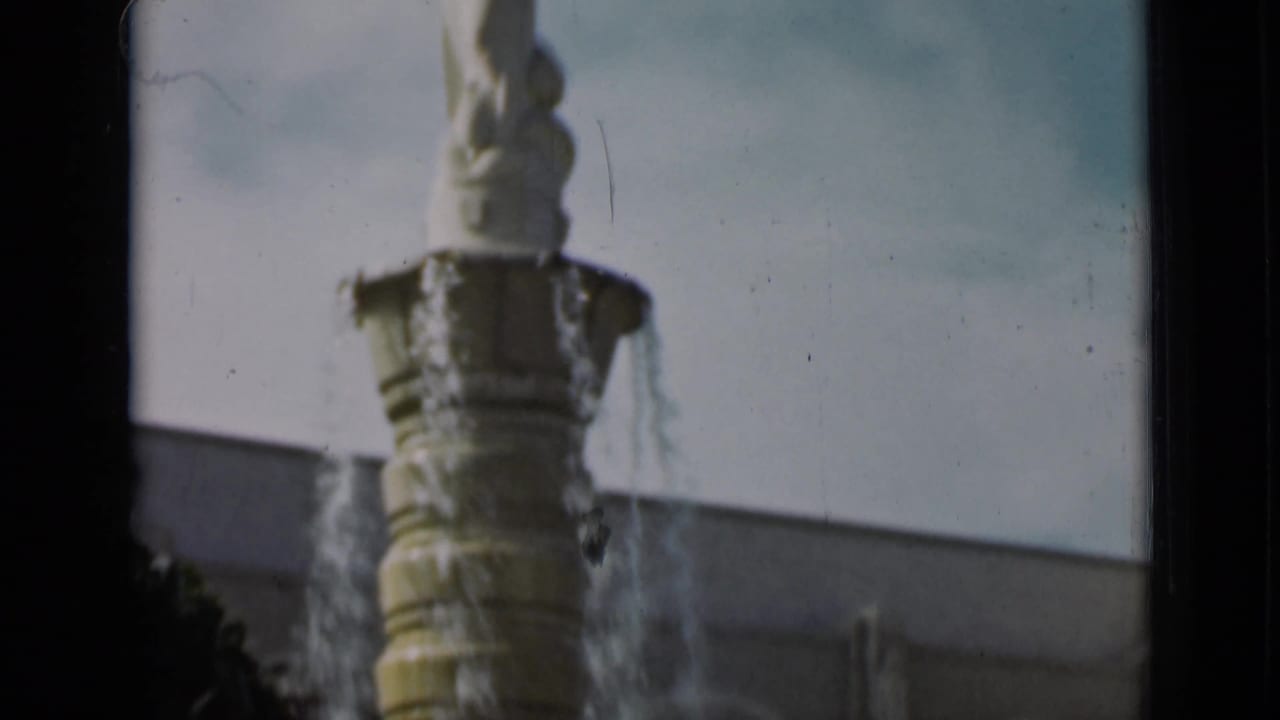 Close 1937 San Francisco frame of an ornate tiered fountain with water jets, pale wall, and soft 8mm focus.