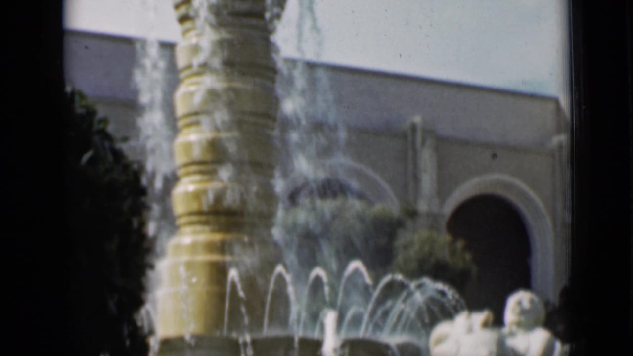 1937 San Francisco home-movie view of a fountain with arcing water, an arched doorway, greenery, and a reclining classical statue.