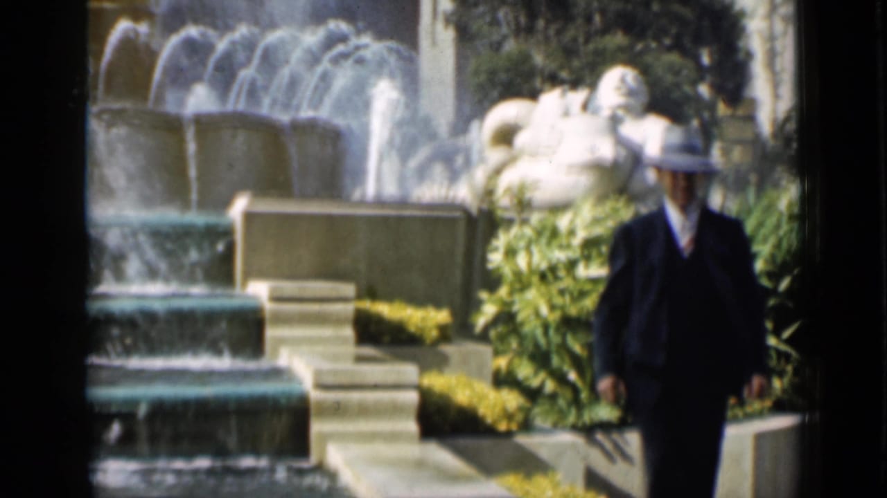 1937 San Francisco footage shows a suited man in a fedora walking past a fountain, white sculpture, planted beds, and steps.