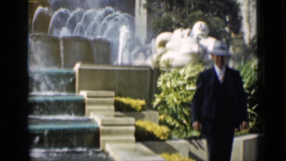1937 San Francisco footage shows a suited man in a fedora walking past a fountain, white sculpture, planted beds, and steps.