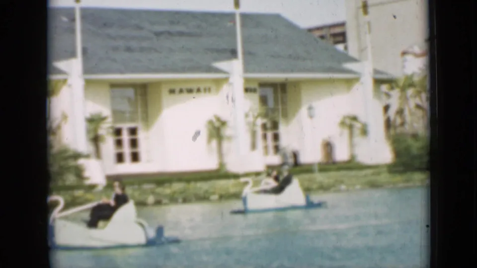 1937 San Francisco park footage shows riders in swan-shaped paddle boats near a white HAWAII building, palms, and water.