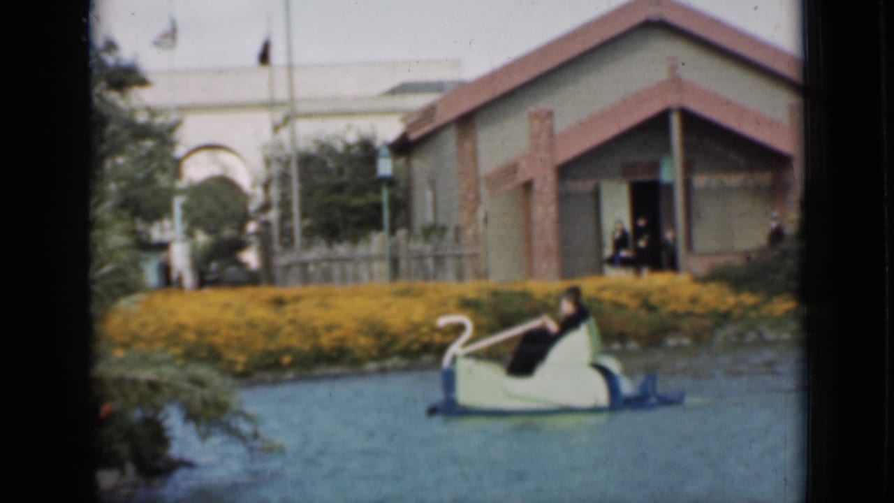 1937 San Francisco home-movie footage shows riders in a swan boat near yellow flower beds, water, and a small lakeside structure.