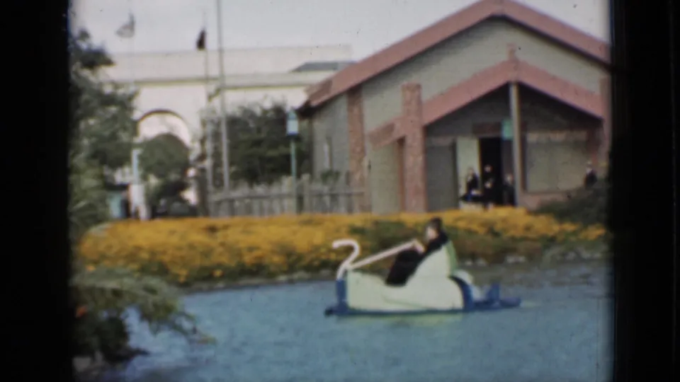 1937 San Francisco home-movie footage shows riders in a swan boat near yellow flower beds, water, and a small lakeside structure.