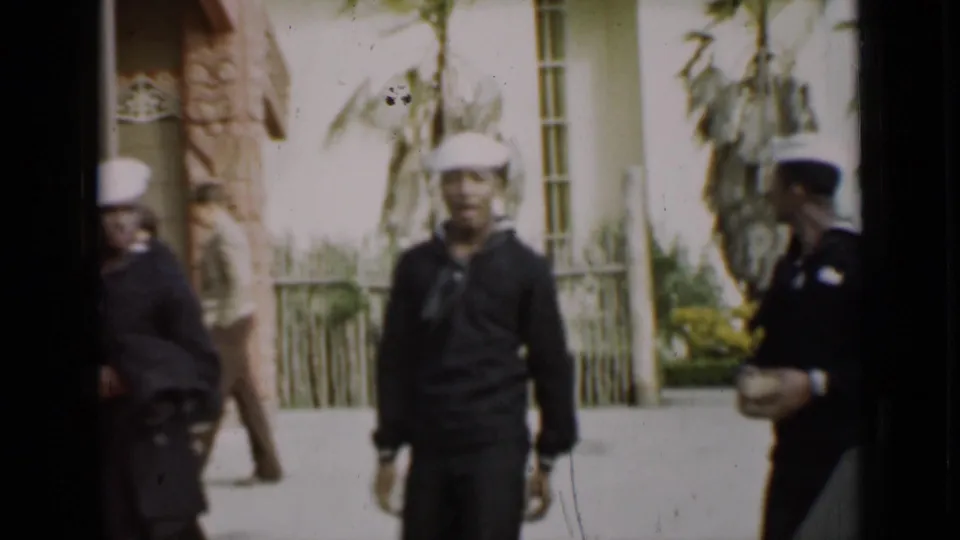 In metadata-supported 1937 San Francisco footage, U.S. Navy sailors pass a landscaped building with palms and decorative stonework.