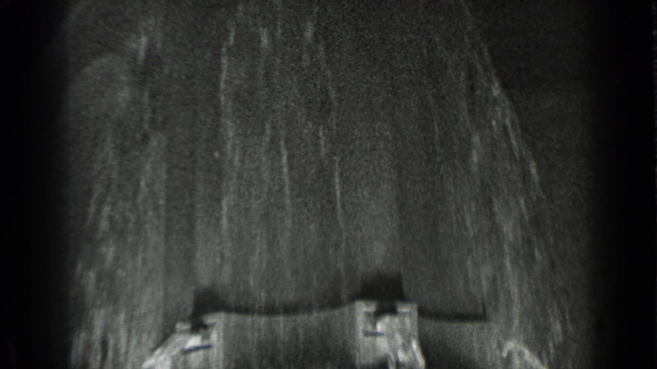Dark, soft-focused frame with a close view of textured film detail and partial structure at the bottom.