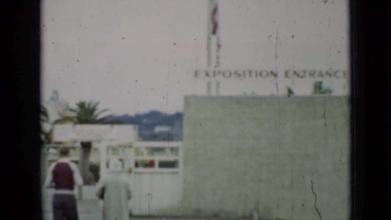 A 1937 San Francisco home-movie frame shows visitors near a concrete wall beneath the "EXPOSITION ENTRANCE" sign.