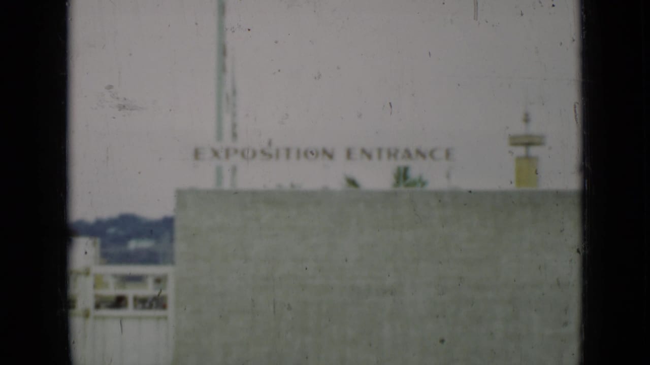 The Exposition Entrance sign and pale concrete wall dominate the frame, with a small view of San Francisco hills and gate structures at left.