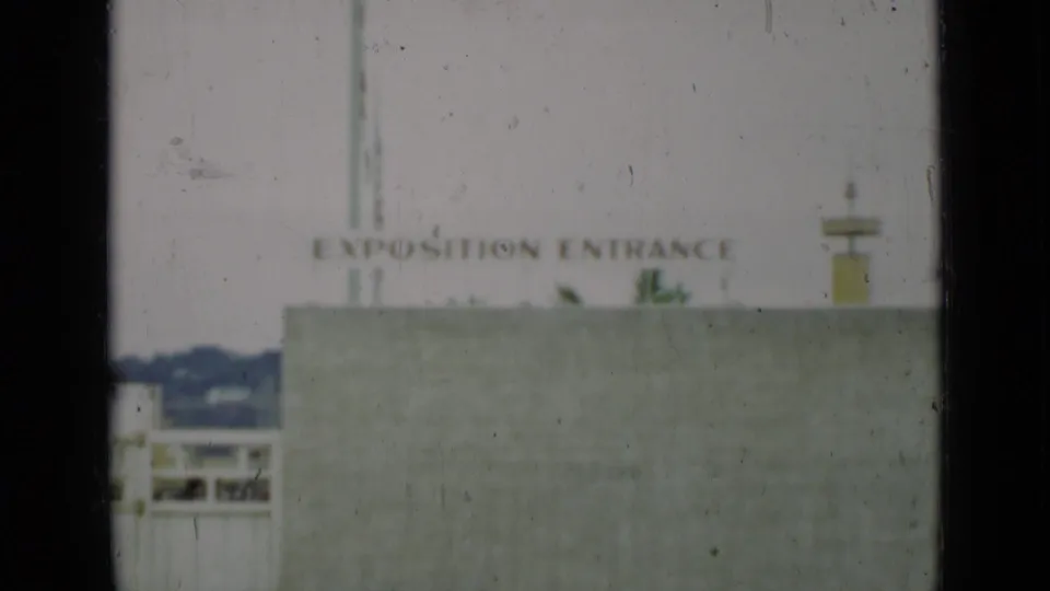 The Exposition Entrance sign and pale concrete wall dominate the frame, with a small view of San Francisco hills and gate structures at left.