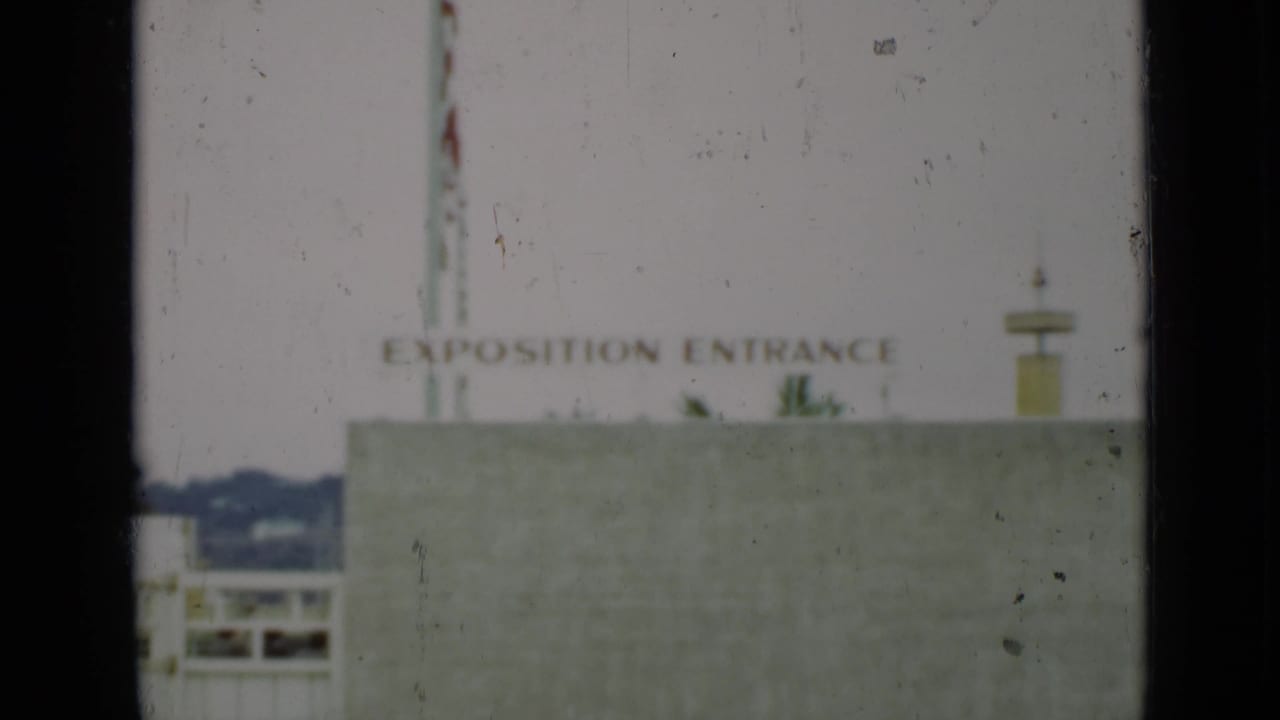 Soft 8mm frame with an Exposition Entrance sign above a pale building.
