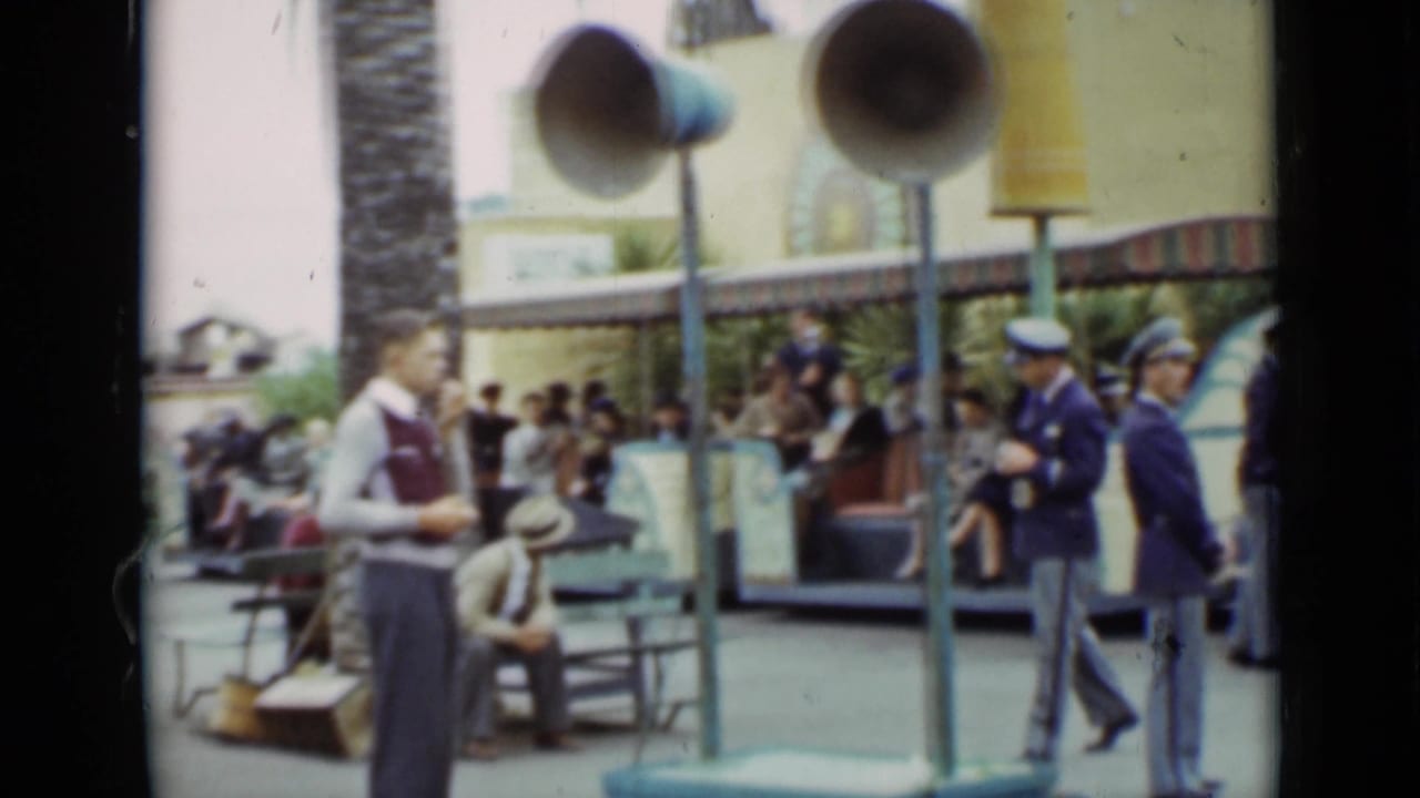 1937 San Francisco park scene showing a vested worker, blue-uniformed attendants, benches, loudspeakers, and guests near an attraction.