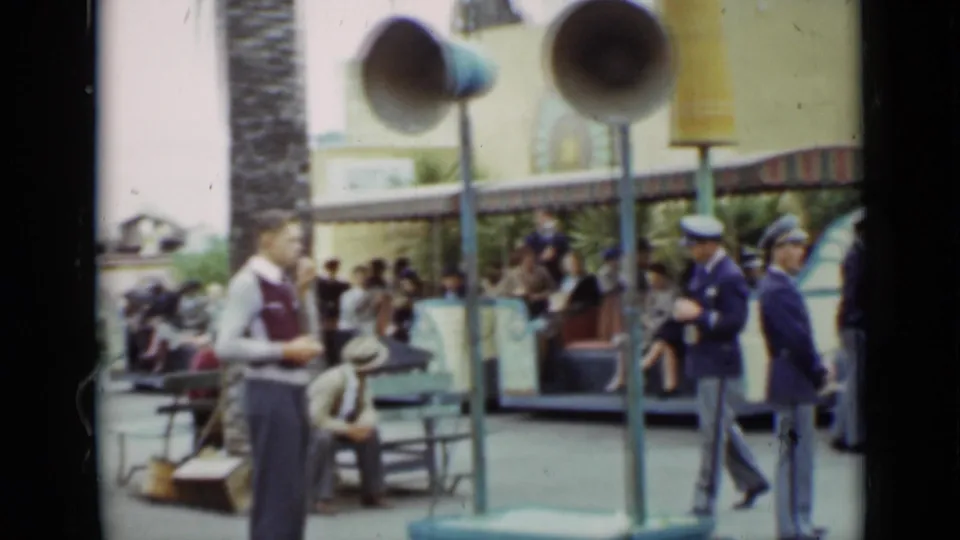 1937 San Francisco park scene showing a vested worker, blue-uniformed attendants, benches, loudspeakers, and guests near an attraction.
