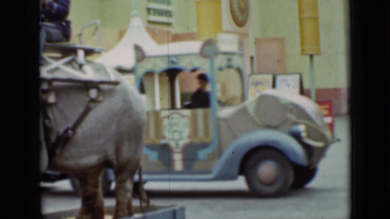 1937 San Francisco home-movie frame showing an elephant ride beside a decorated vehicle with a striped canopy and a few visible people.