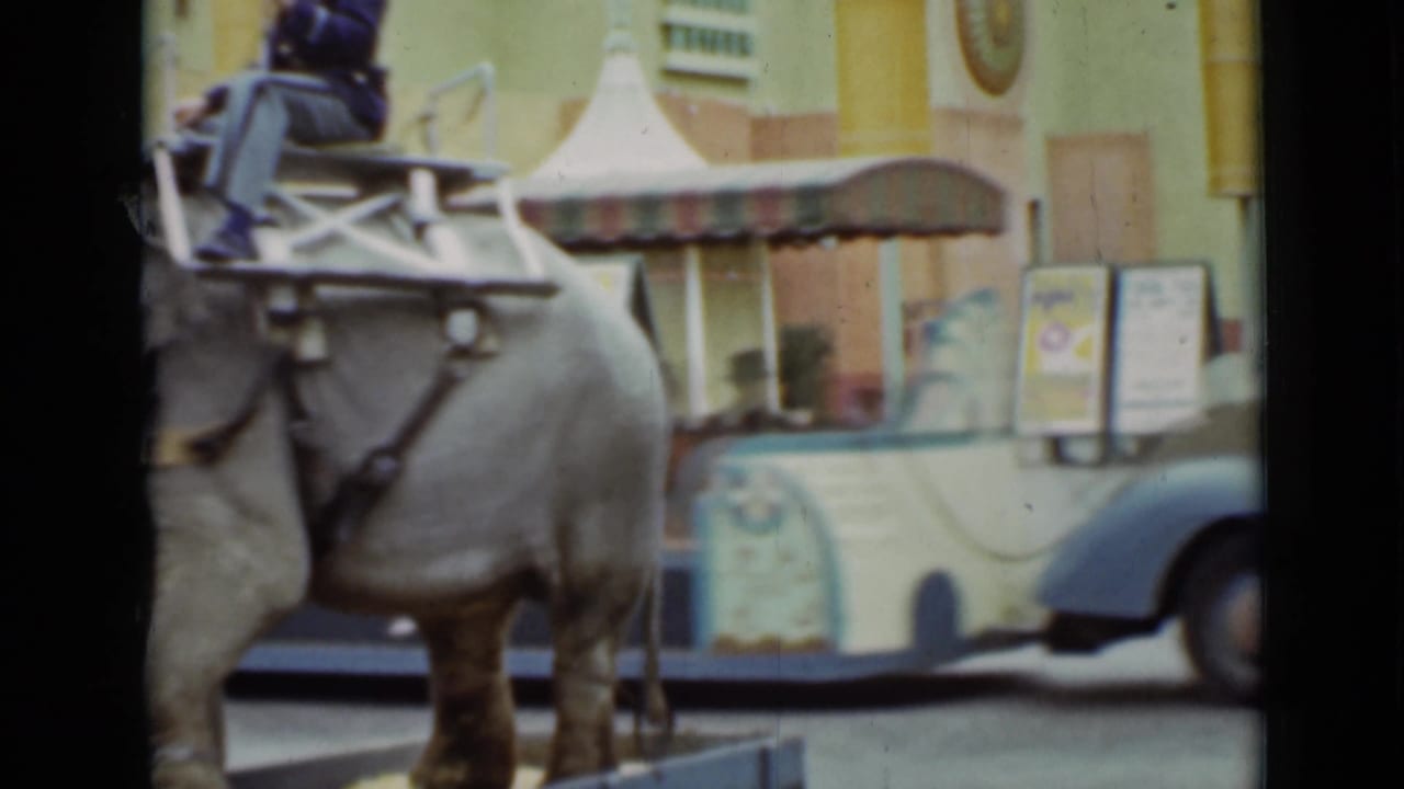 The elephant fills the foreground as a colorful ornate vehicle with a striped canopy stands behind it in this 1937 San Francisco frame.