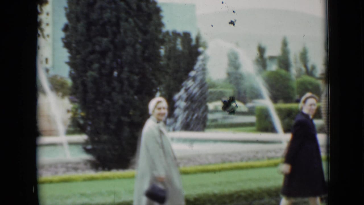 Two adult women in coats stand or walk near the garden fountain, with one woman turning toward the camera in the supported 1937 San Francisco setting.