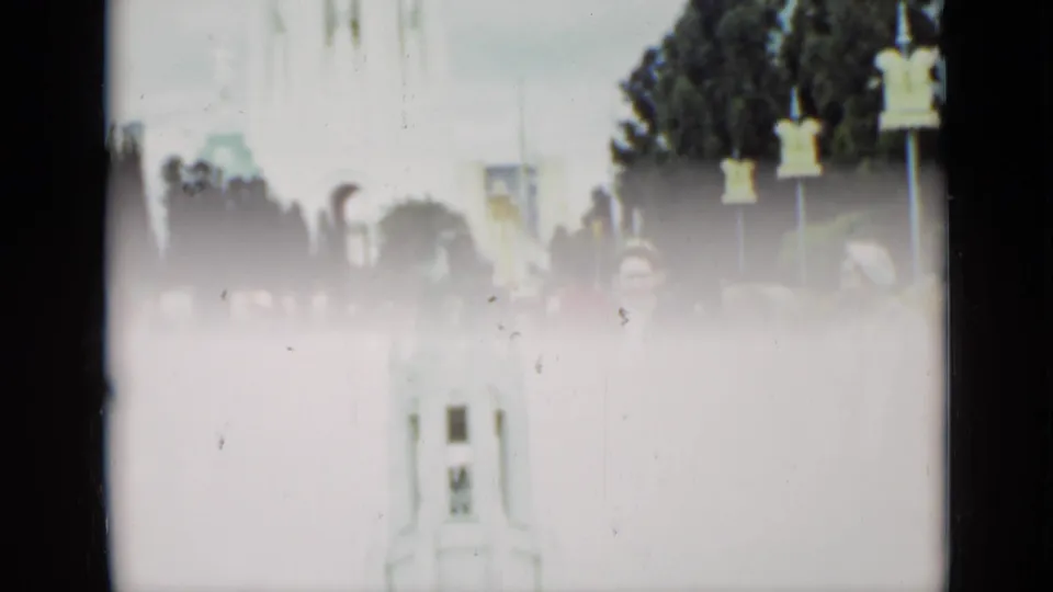 1937 San Francisco home-movie frame showing people near a pale tower or monument in a landscaped urban square.