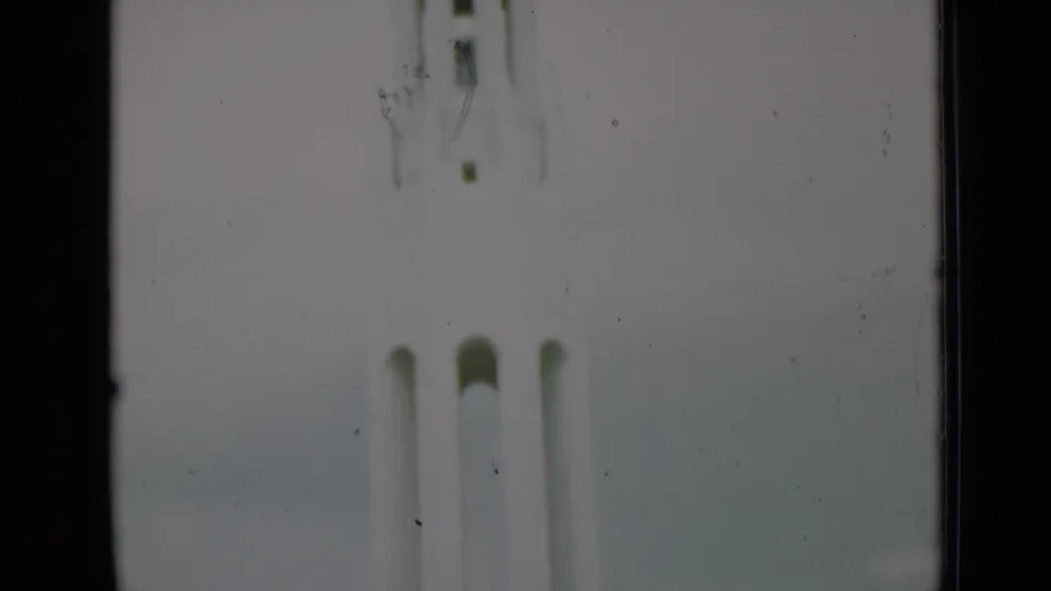 Overexposed 8mm frame showing the base and vertical forms of a pale civic monument in the San Francisco clip.
